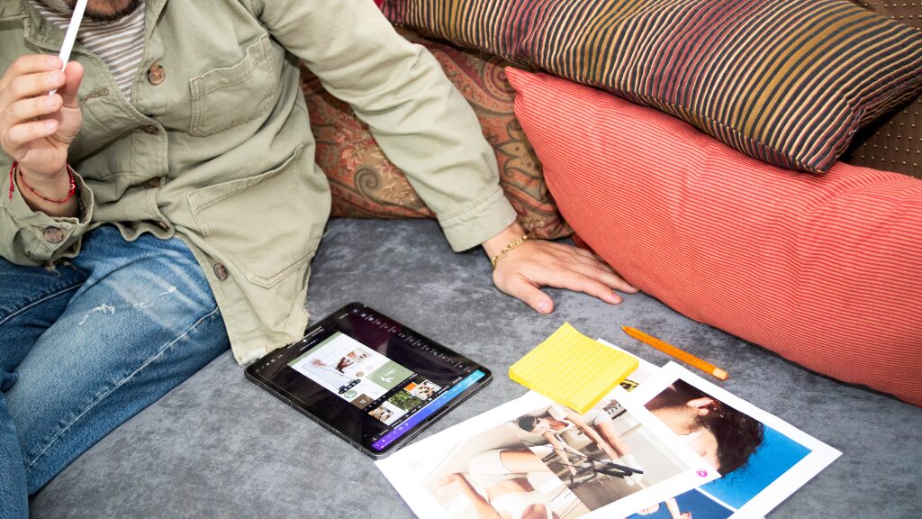 Personne travaillant sur une tablette avec des supports visuels et des notes de travail à proximité.