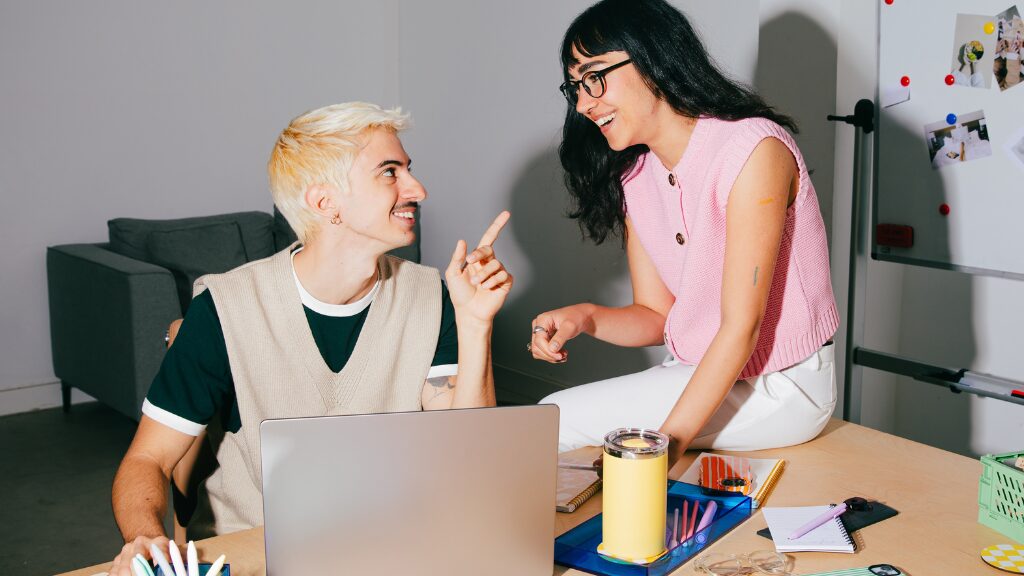 Deux étudiants discutant autour d’un ordinateur portable dans une salle de travail collaborative.